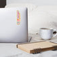Laptop with chalet bar-b-q sticker on a bed next to a notebook and mug