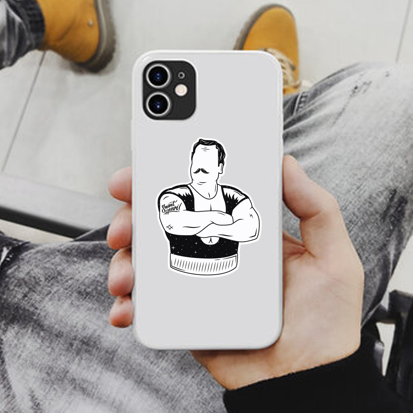 Person holding a white phone case with a black and white sticker of louis cyr on a couch.