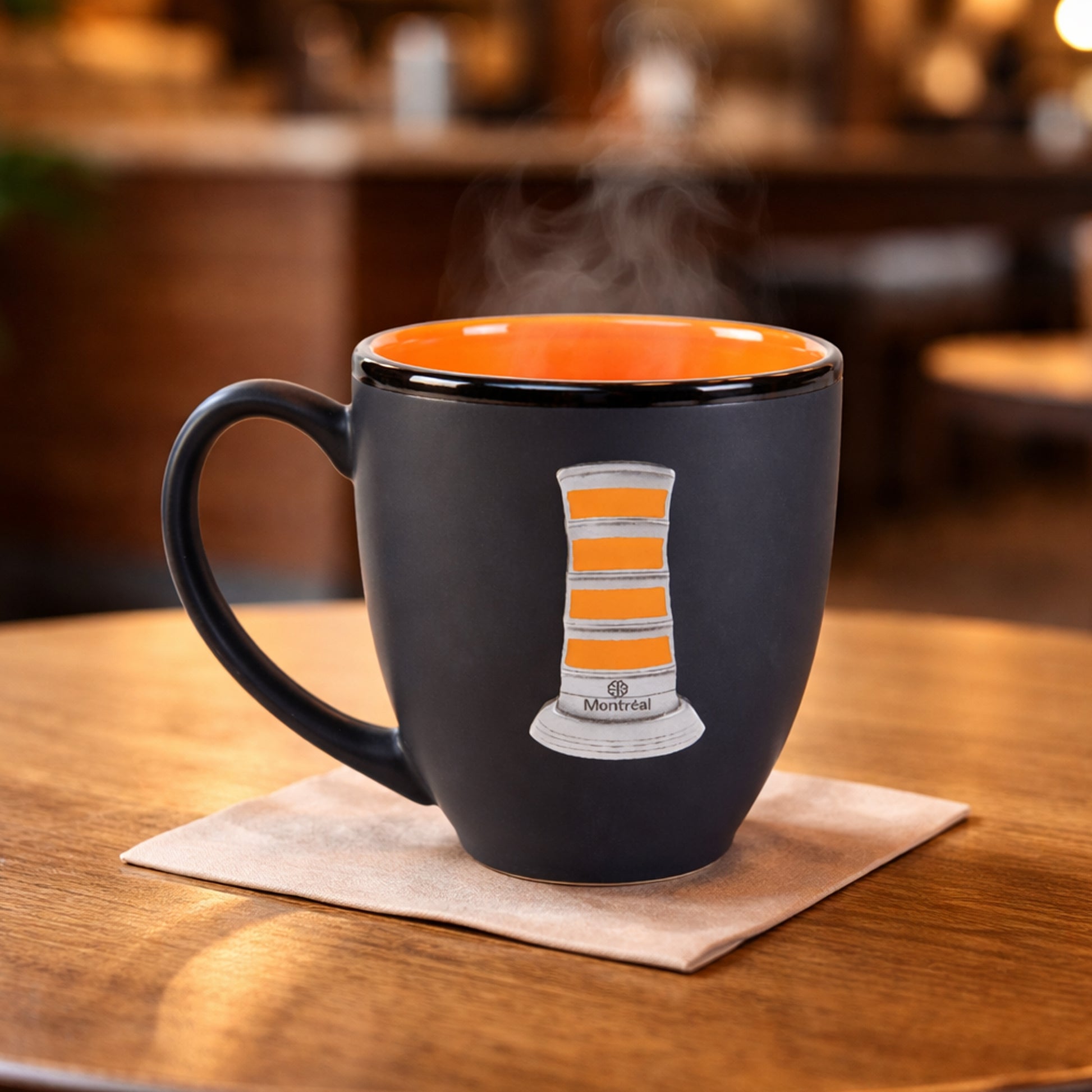 Black mug with orange interior, featuring a orange cone mug crest, on a wooden table with steam rising.