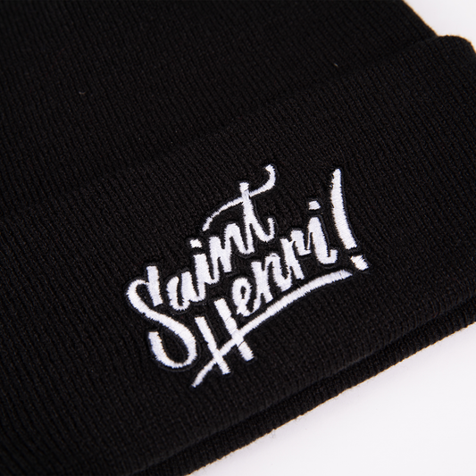 A closeup of a black tuque with the Saint-Henri design embroidered on the front. 